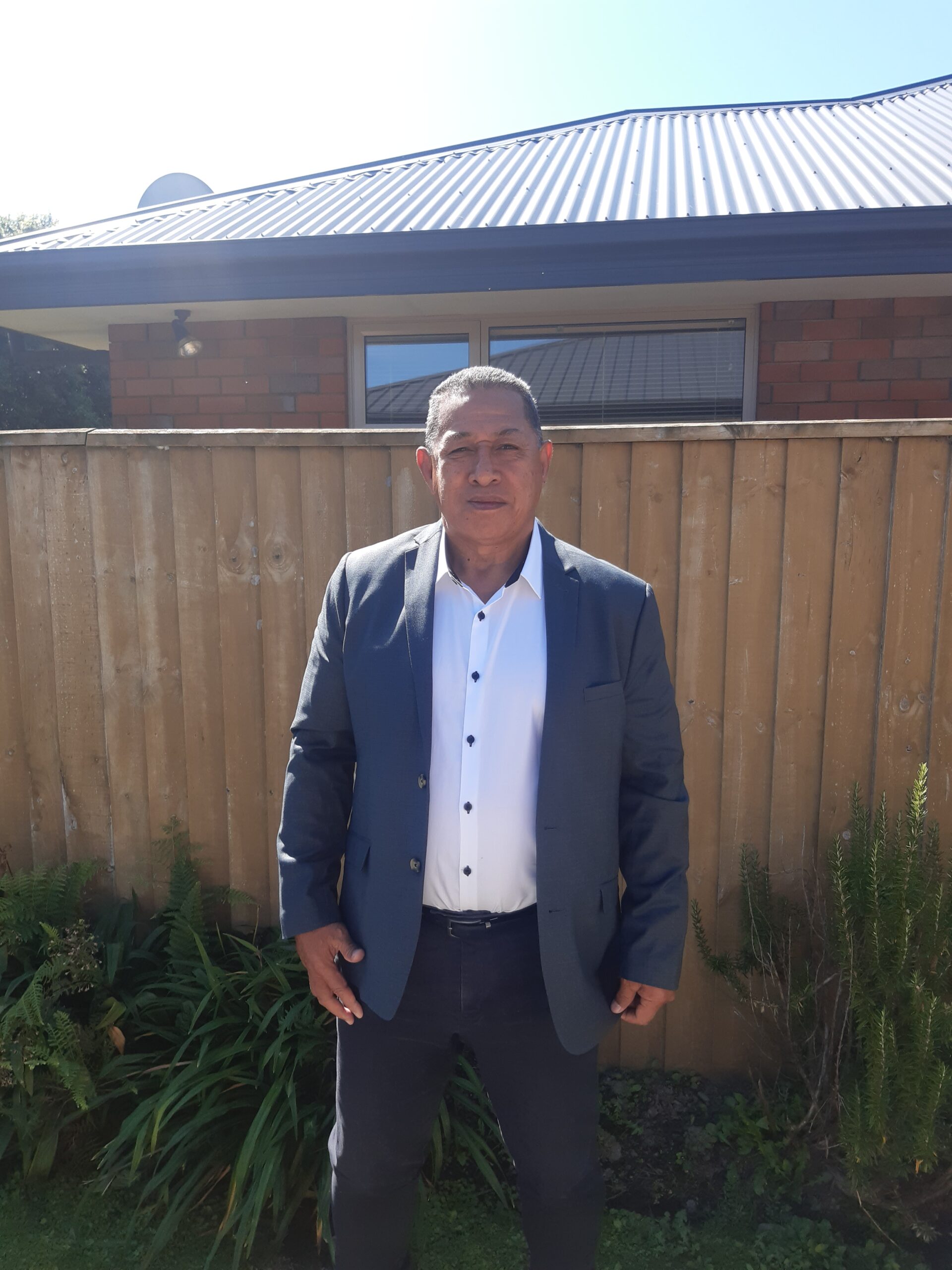polynesian man standing in front of a wooden fence